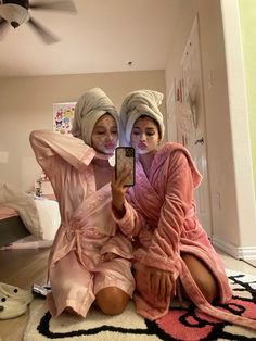 two women in pink robes taking a selfie with their cell phone while sitting on the floor