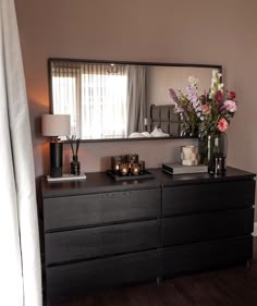 a black dresser with flowers and candles on it in front of a large mirror above the dresser