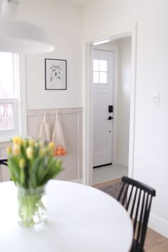 a white dining room table and chairs with flowers in the vase on the table next to it