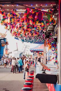 a carnival filled with lots of people and colorful balloons hanging from the ceiling above them