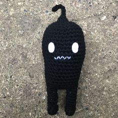 a crocheted black stuffed animal with eyes and mouth is on the ground next to a sidewalk