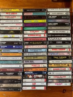 a collection of various cd's are stacked up on a wooden shelf in front of a wall