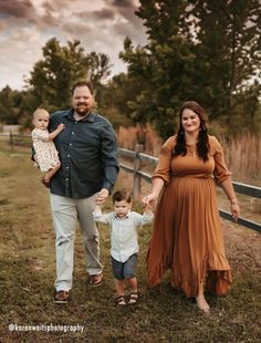 a man and woman hold hands as they walk with their toddler in an open field