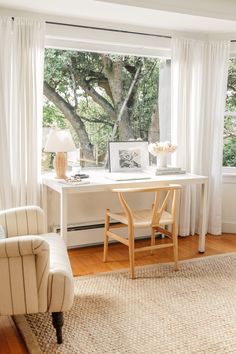 a white desk and chair in front of a large window with curtains on the windowsill