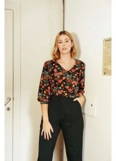 a woman standing in front of a white door wearing black pants and a floral blouse