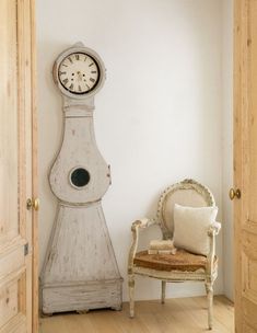 an old grandfather clock sitting in the corner of a room next to a white chair