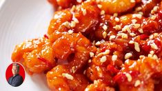 a white plate topped with chicken covered in sauce and sesame seed flakes next to a man's face