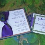 two wedding cards with peacock feathers and purple ribbon on the front one is folded in white paper