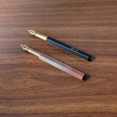 two fountain pens sitting on top of a wooden table next to each other, one black and the other gold