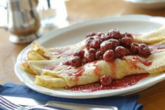 a white plate topped with crepes covered in red sauce and beans next to silverware