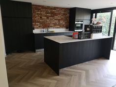 a kitchen with black cabinets and an island in the middle of it, next to a brick wall