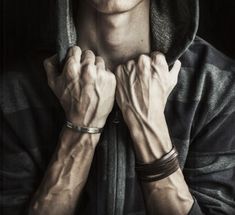 a man in a hoodie with his hands on his chest and wearing bracelets