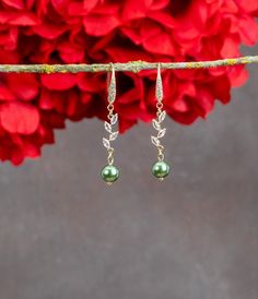 two green pearls hanging from a branch with red flowers in the backgrounnd