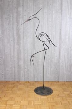 a metal flamingo standing on top of a wooden floor next to a white wall