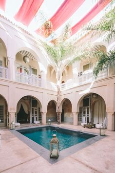 an indoor swimming pool in the middle of a building with palm trees and chairs around it