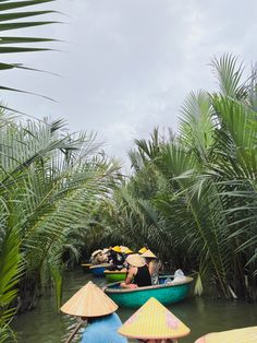 several people in small boats with umbrellas floating down a river surrounded by palm trees