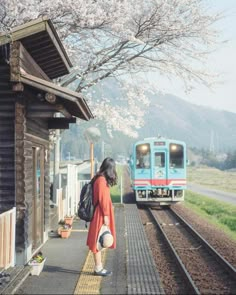 a woman in an orange dress is waiting for the train to pass by on the tracks