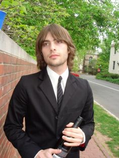 a man in a suit and tie standing next to a brick wall holding a bottle