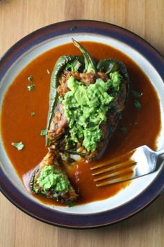 a white plate topped with stuffed peppers covered in sauce and guacamole next to a fork