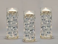 two clear glass vases with silver balls and lights on the bottom one has a white candle in it