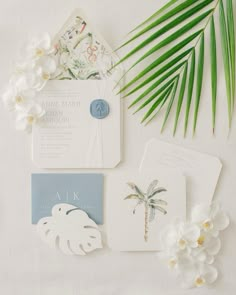 the wedding stationery is laid out with palm leaves, flowers and other things to put on it