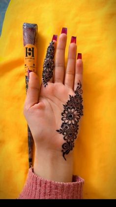 a woman's hand with henna on it next to a yellow pillow and a ruler