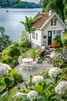 a small white house sitting on top of a lush green hillside next to a lake