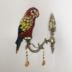 a colorful bird sitting on top of a wall light next to a lamp fixture with beads hanging from it's sides