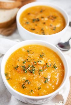 two white bowls filled with soup sitting on top of a table next to slices of bread