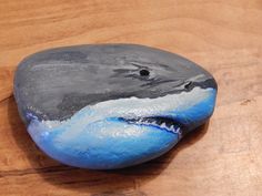 a painted rock sitting on top of a wooden table covered in blue and gray paint