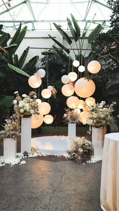 an arrangement of flowers and paper lanterns hanging from the ceiling in a room filled with greenery