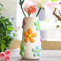 a vase with flowers painted on it sitting on a table next to some pink roses