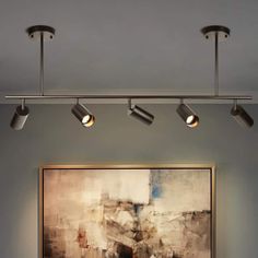 an abstract painting hangs on the wall next to three lights in a room with gray walls