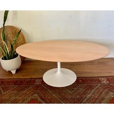 an oval wooden table sitting on top of a rug next to a potted plant