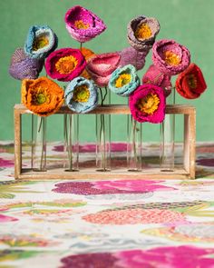 several crocheted flowers are placed in vases on a floral tablecloth with a green background