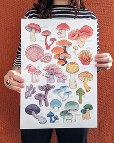 a woman holding up a poster with different mushrooms on it's front and back