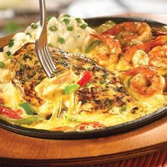 a pan filled with shrimp and mashed potatoes on top of a wooden table next to a fork