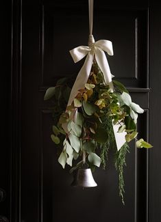 a bell hanging from the side of a black door with greenery and white ribbon