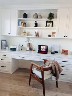 a white desk topped with a computer monitor next to a shelf filled with books and vases