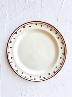 an empty white plate with red trim on a white wall behind it is a brown border around the edge