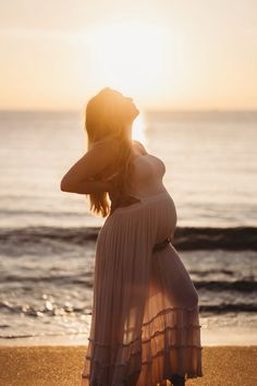 a pregnant woman standing on the beach at sunset