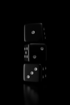 two black dices sitting on top of each other in front of a black background