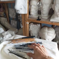 a person's hand on top of some art supplies in front of white busturines