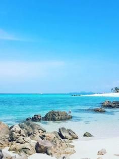 the beach is full of rocks and clear blue water, with an island in the distance