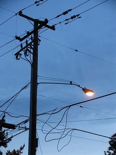 an electric pole and street light in the evening with power lines running across the sky