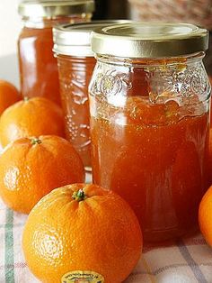 some oranges are sitting on a table next to jars with jam in them,