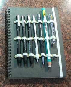 several pens and pencils are lined up on a notebook