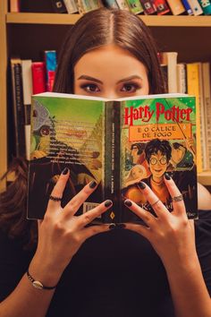 a woman holding up a harry potter book in front of her face with both hands