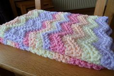 a crocheted blanket sitting on top of a wooden table next to a chair