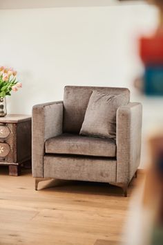 a chair sitting on top of a hard wood floor next to a vase with flowers